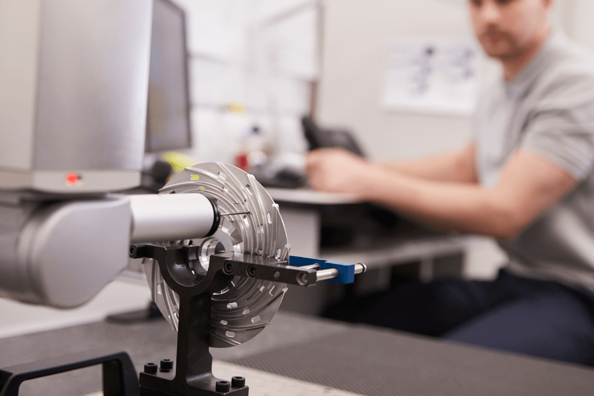 Ein Messtechniker arbeitet an einem Prüfstand mit einem präzisen Messinstrument, das eine metallische Komponente analysiert.