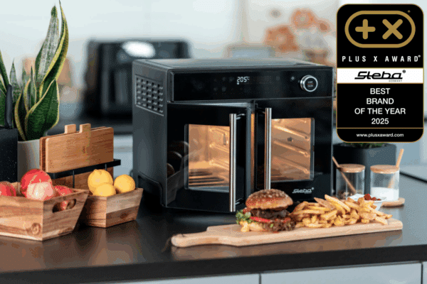 Steba Elektrogerät mit zwei Türen, Award-Auszeichnung, umgeben von frischen Lebensmitteln und Küchenutensilien.