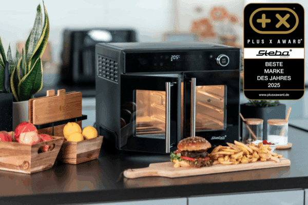 Airfry-Grillbackofen AF 24 TRI-ZONE von Steba auf einer Kücheninsel umgeben von Dekoration mit einem Hamburger und Pommes im Vordergrund. An der rechten Seite befindet sich ein Plus X Award, der Steba als Beste Marke des Jahres 2025 auszeichnet.