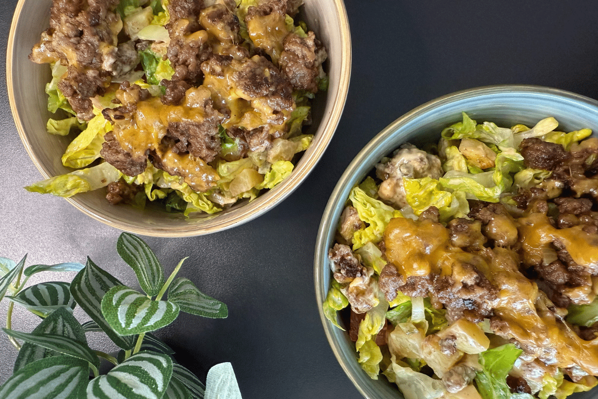 Zwei Schalen mit Cheeseburger-Salat, bestehend aus Hackfleisch, geschmolzenem Cheddar, knusprigen Kartoffelwürfeln, Gurken, Tomaten und frischem Salat