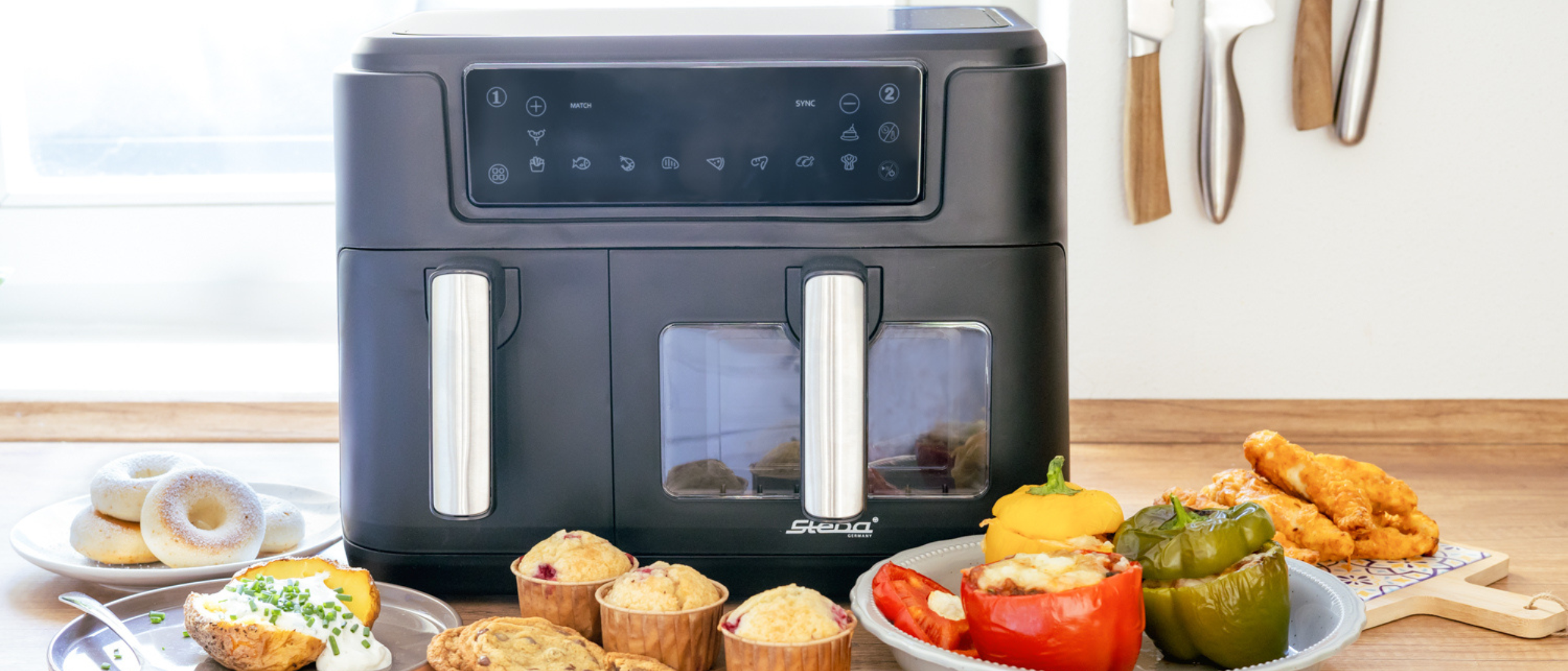 Heißluftfritteuse HF 9500 DUO mit einer Variation an Gerichten, die mit diesem Gerä zubereitet wurden, Auf dem Bild befinden sich gefüllte Paprika, Muffins, Cookies und eine Ofenkartoffel mit Sour Creme getoppt.