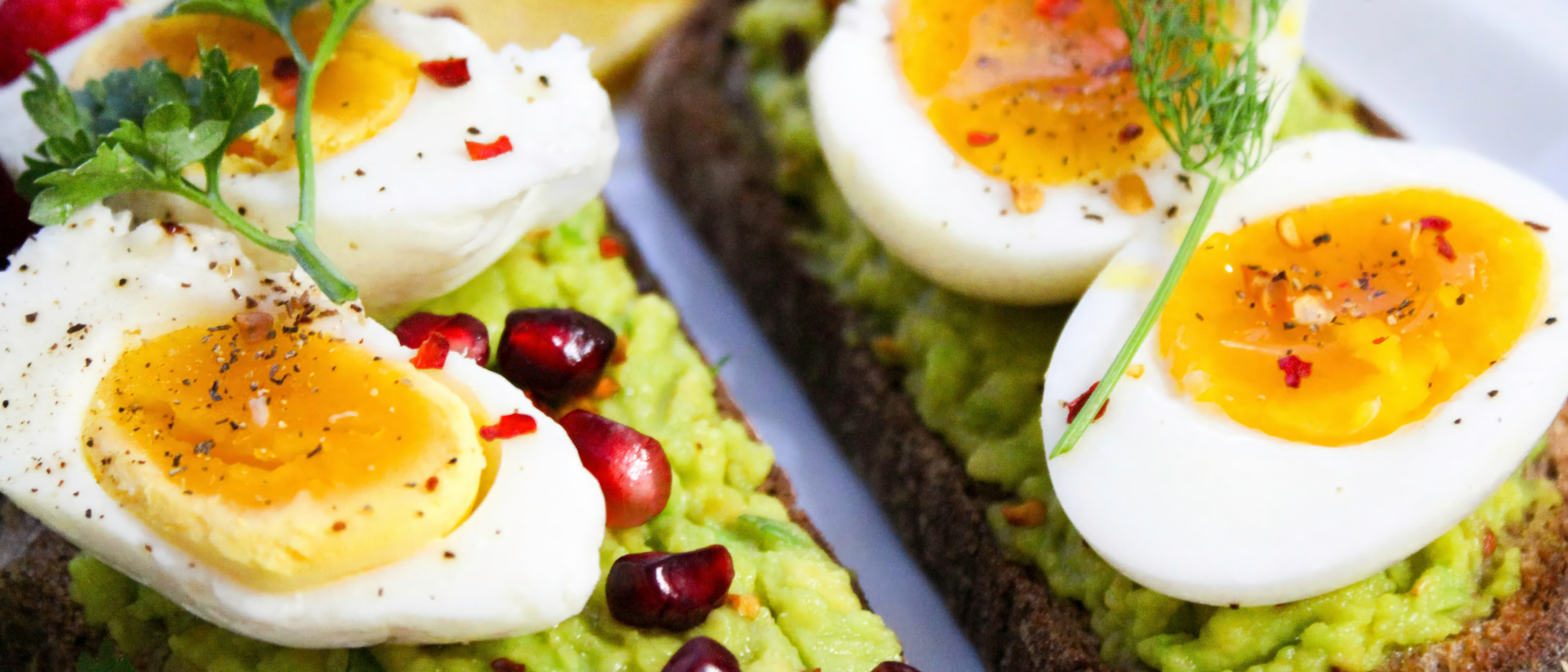 Aufgeschnittene, mittelgekochte Eier auf einem Avocadobrot, garniert mit Gewürzen und Granatapfelkernen.