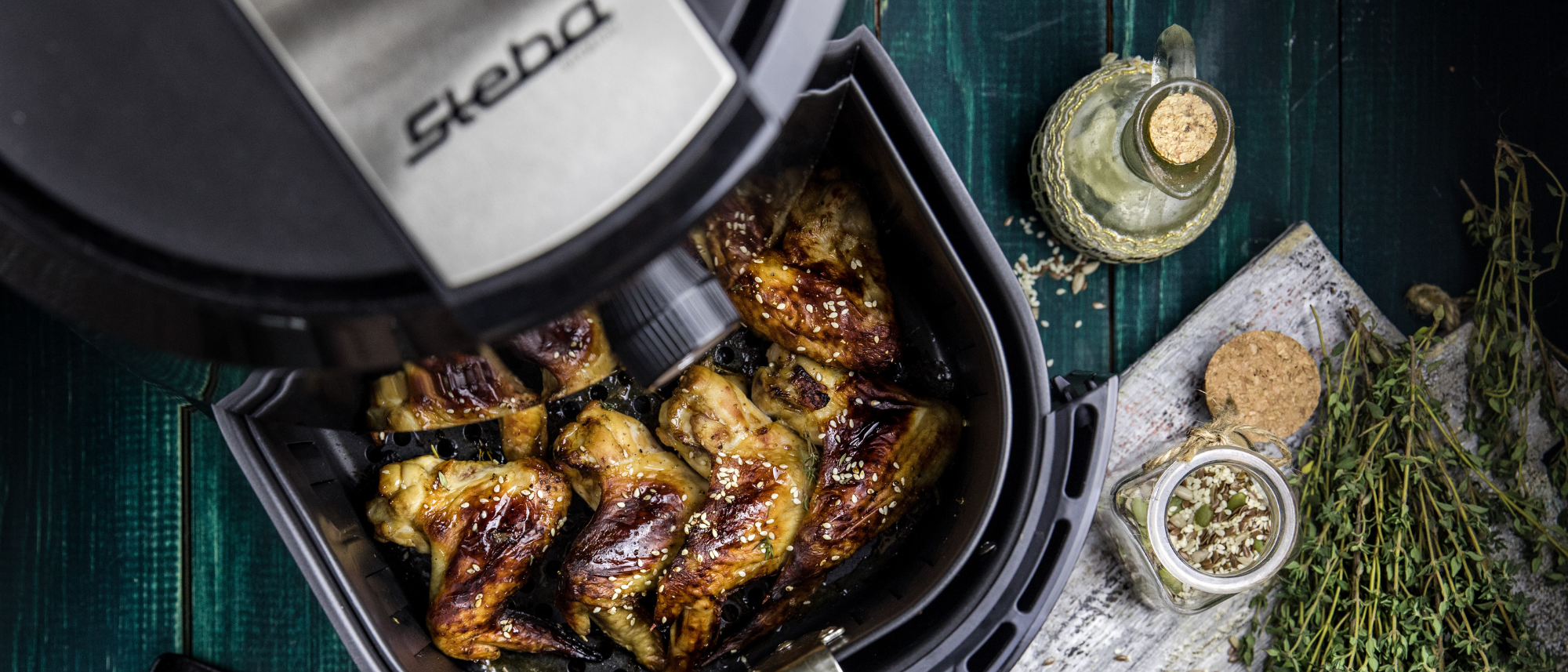 Heißluftfritteuse HF 5000 mit herausgezogenem Korb und knusprig gebratenen Chicken Wings.