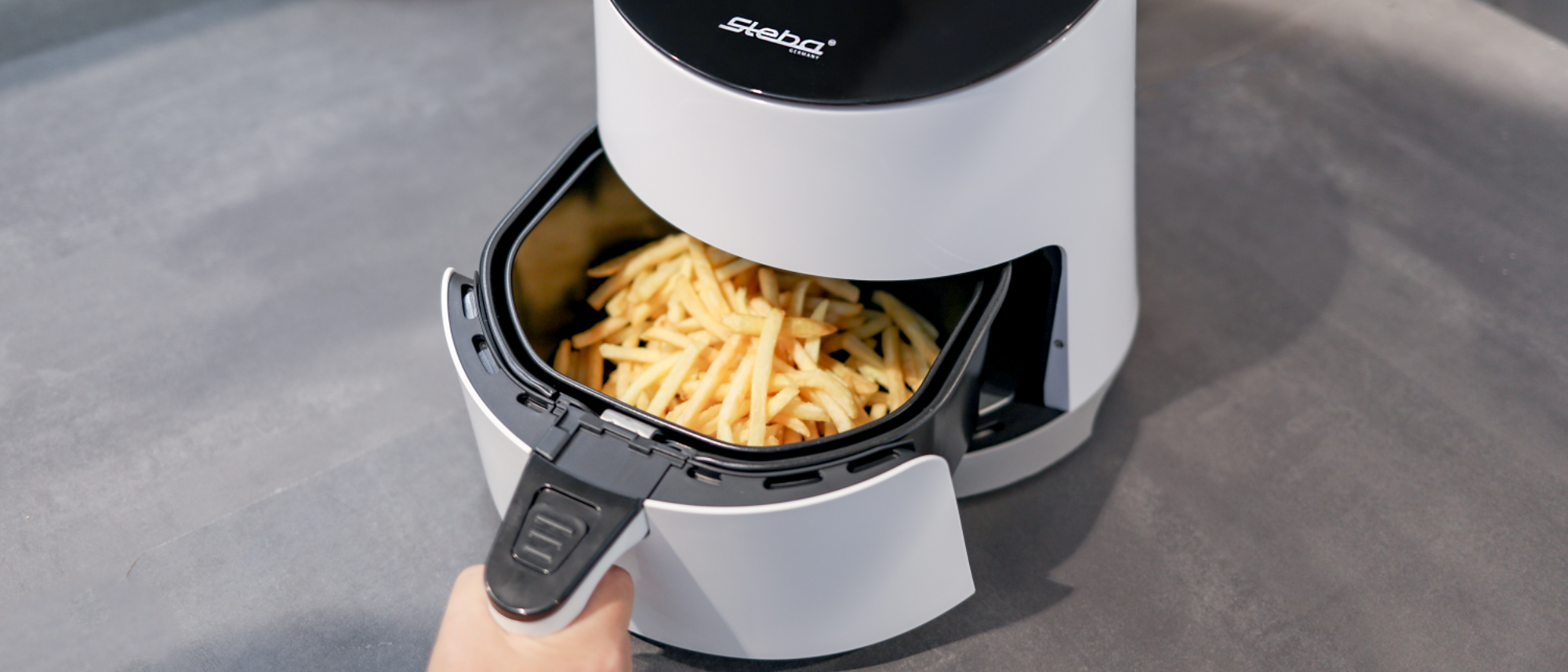 Heißluftfritteuse HF 1000 mit offenen Korb, der mit knusprigen Pommes gefüllt ist.